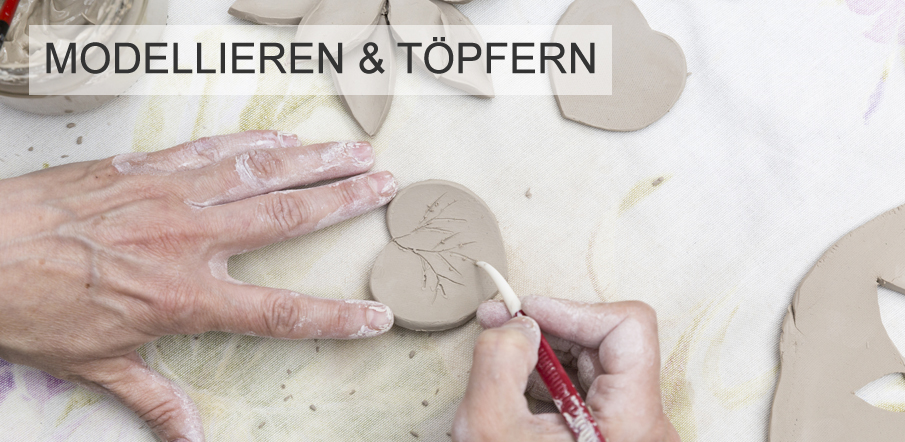 Zwei Hnde bearbeiten Ton: Eine Hand hlt ein Tonstck in Herzform, die andere ritzt mit einem Modellierwerkzeug ein filigranes Astmotiv hinein. Oben im Bild steht der Text 'Modellieren & Tpfern'.
